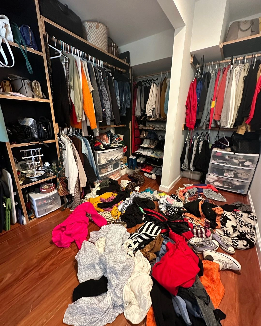 Walk-in closet buried in clothes thrown across the wooden floor and racks packed tight