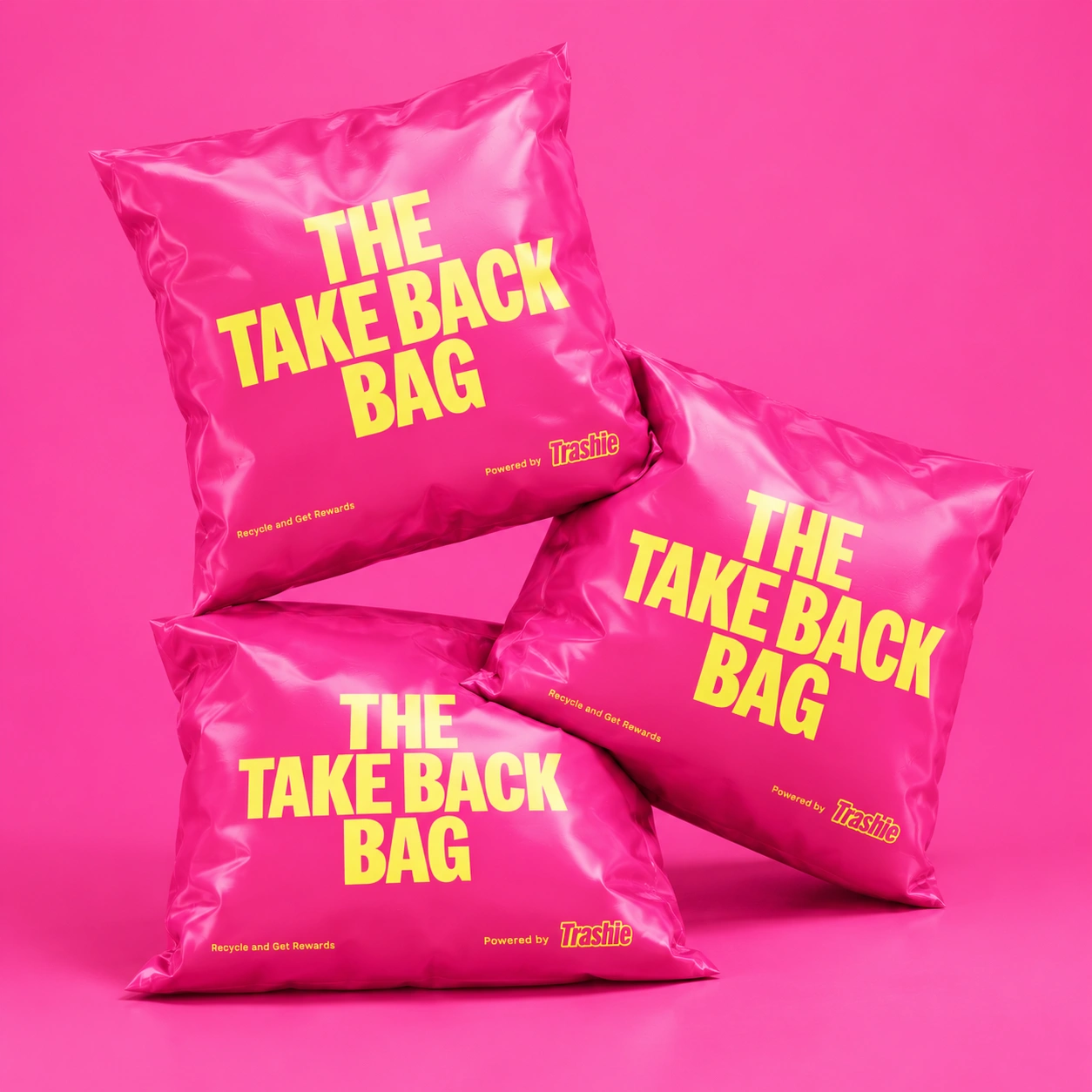 Three pink Take Back Bags printed with THE TAKE BACK BAG in yellow, stacked on a pink background